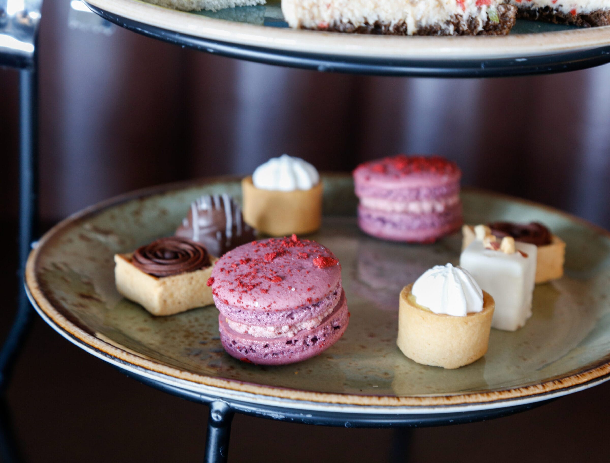 A tiered plate featuring colorful macarons, mini pastries, and chocolate treats, set against a dark background.